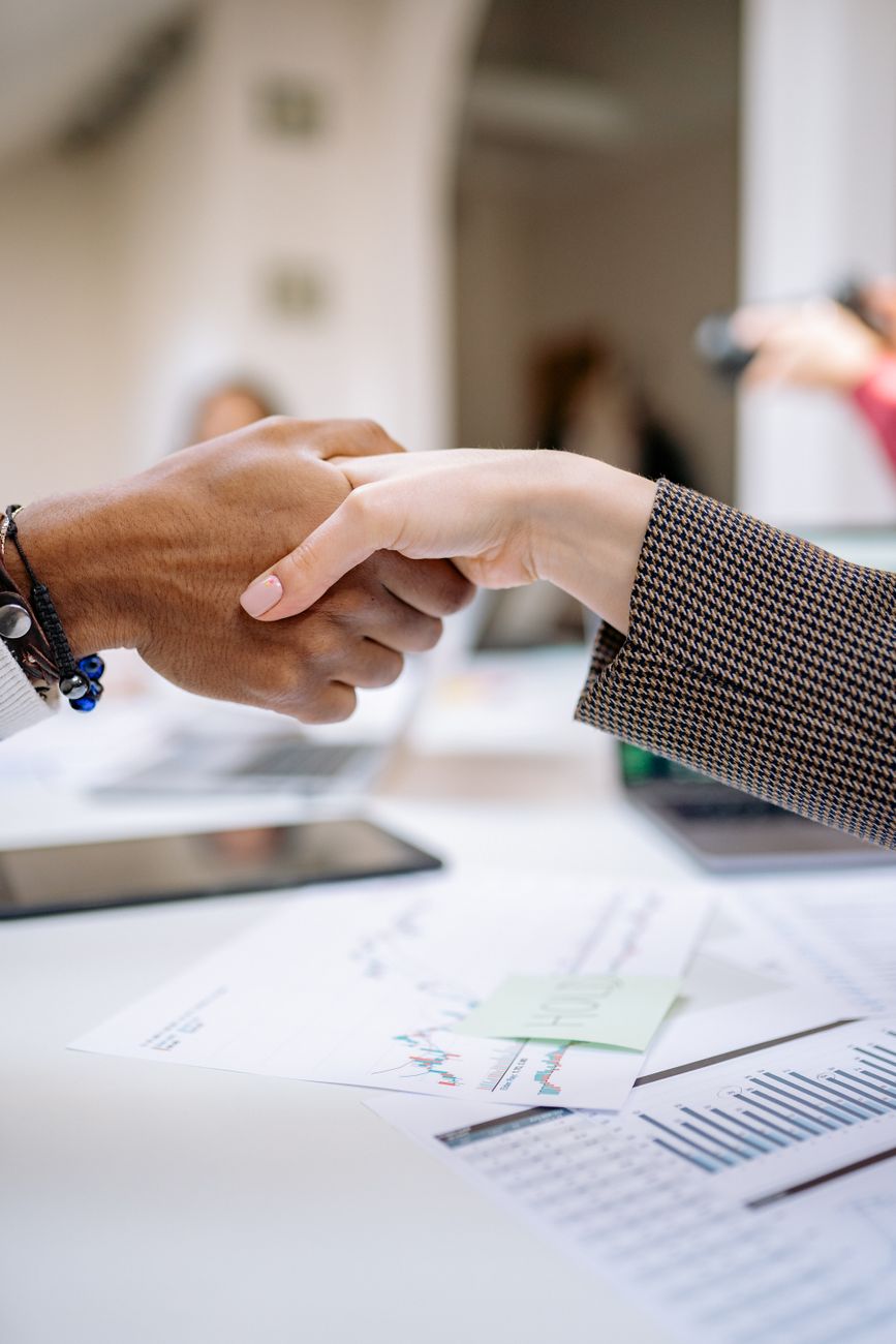 Two people shaking hands over a desk of printed charts