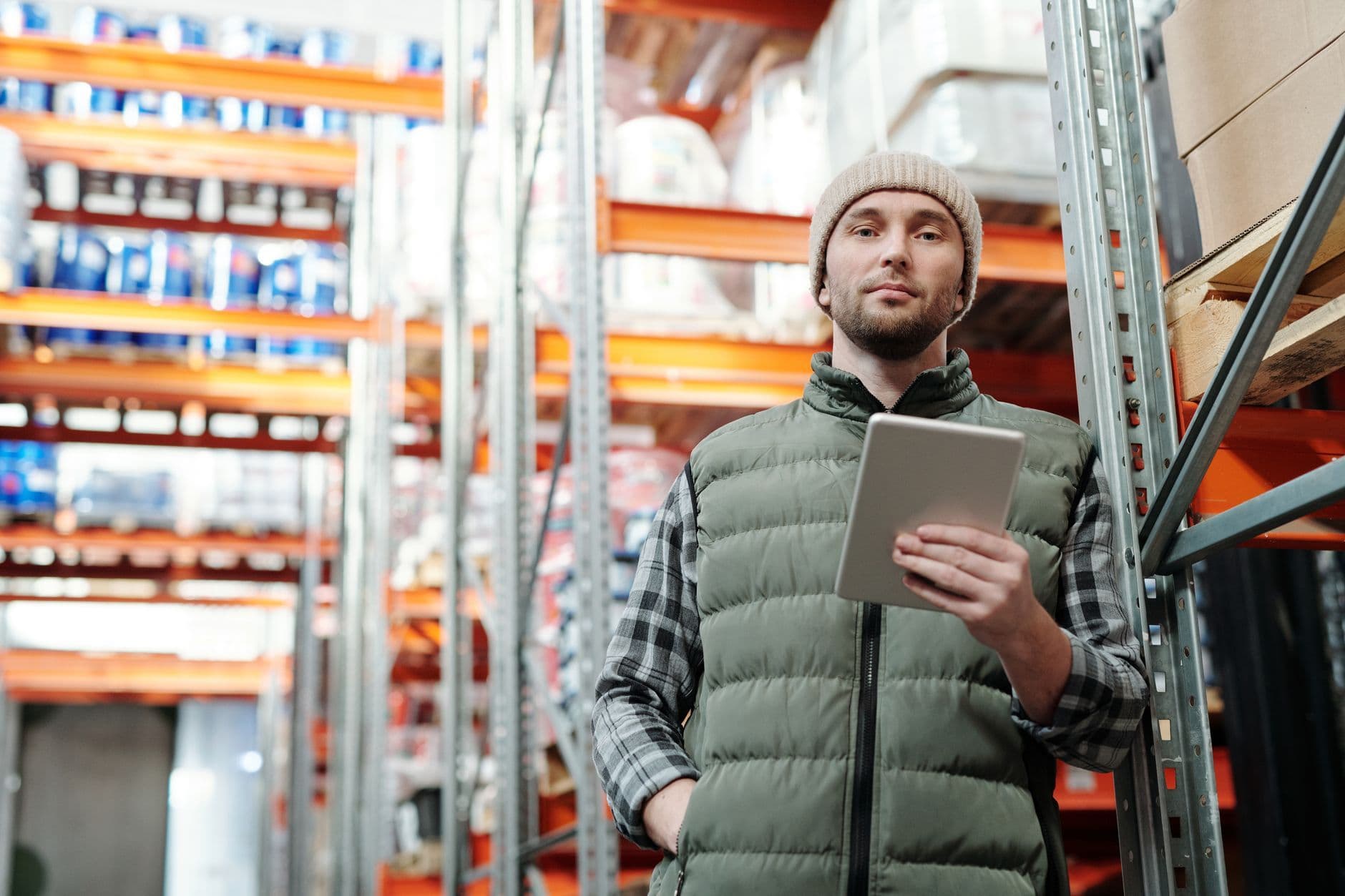 A warehouse manager reviewing inventory on a tablet beside racking